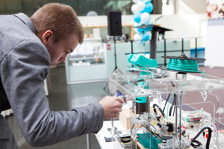 Олег Зобов демонстрирует модель промышленного робота и создавший её 3D-принтер.